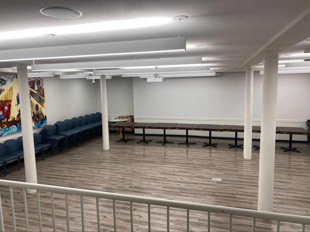 Middle Church Social Hall in an open room layout, with tables folded along the wall and chairs stacked to one side beneath the community murals